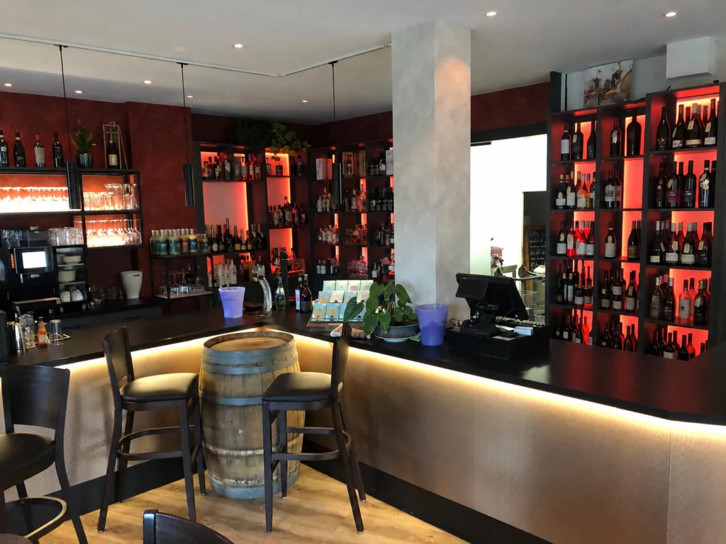 Theke mit Weinfass und Barstühlen, dahinter rot hinterleuchtete Weinregale.