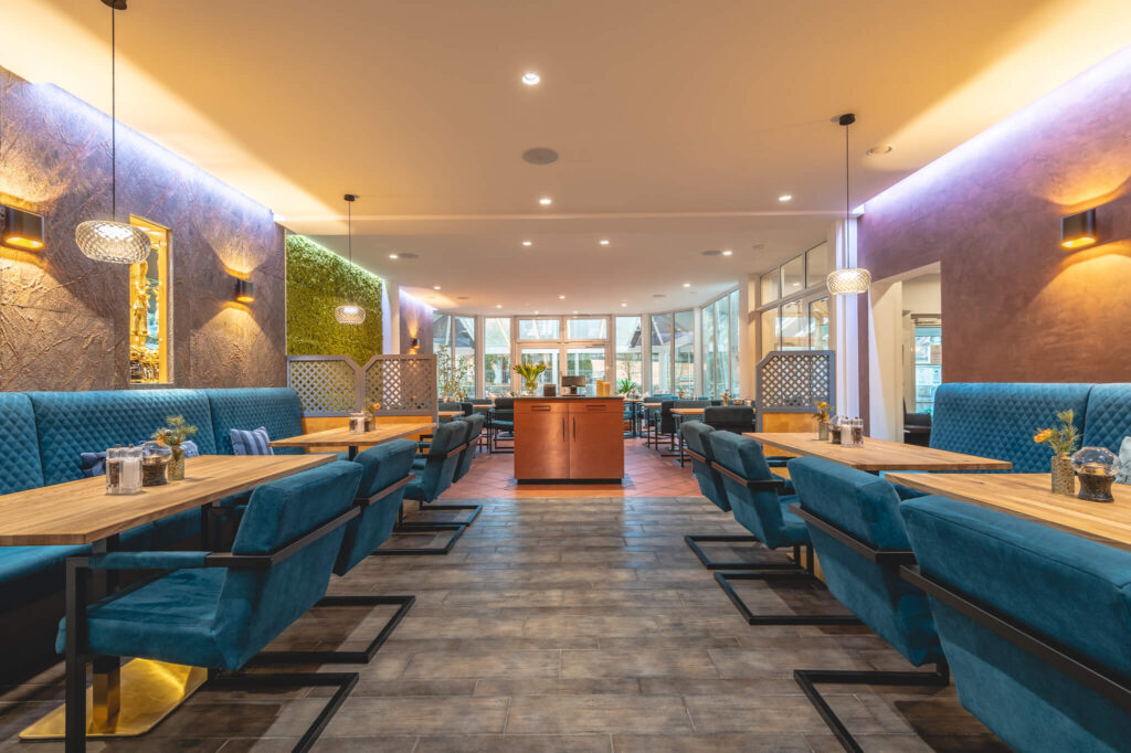 Restaurant mit petrolfarbenen Samtbänken und Holztischen.