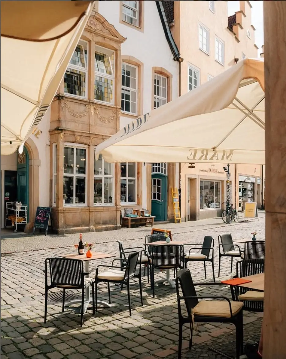 Außenterrasse mit Bistrostühlen und Sonnenschirmen in einer Altstadtgasse.
