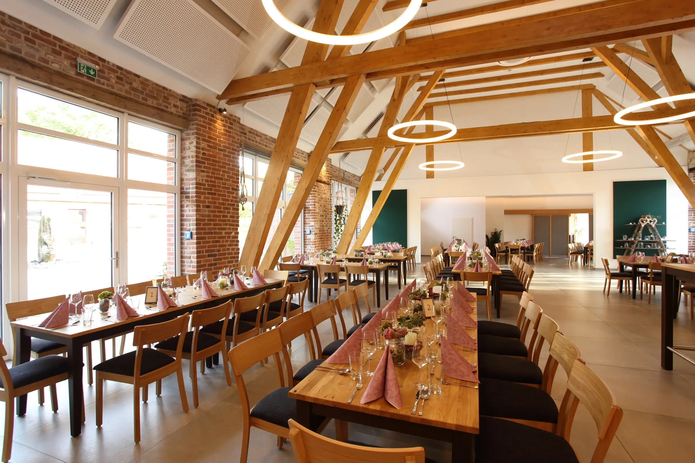 Festsaal mit Holzbalkendecke, langen eingedeckten Tafeln und Holzstühlen.